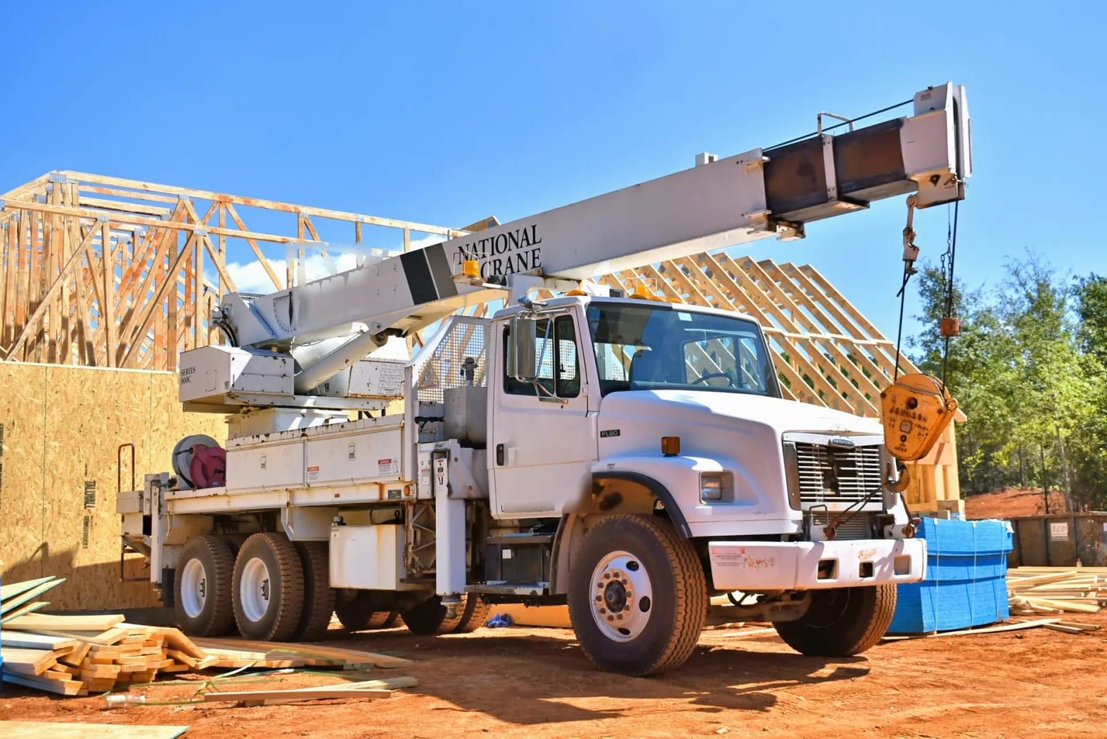 White boom truck crane parked beside a house frame, boom raised