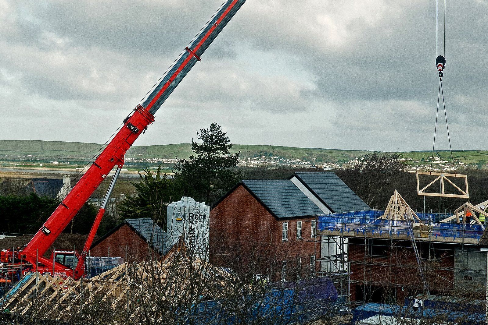 A telescopic mobile crane lowering a roof truss onto new brick houses