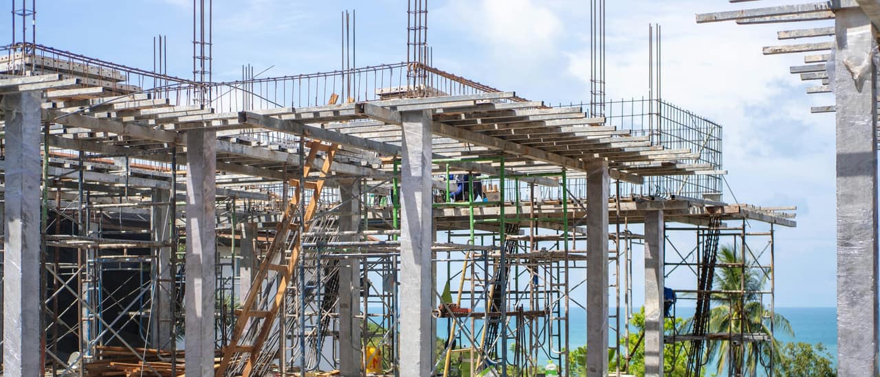 Concrete building going up behind palm trees, with the Gulf in the distance