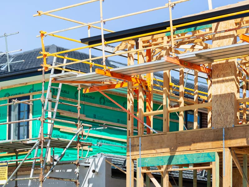 House under construction with scaffolding and wood roof framing
